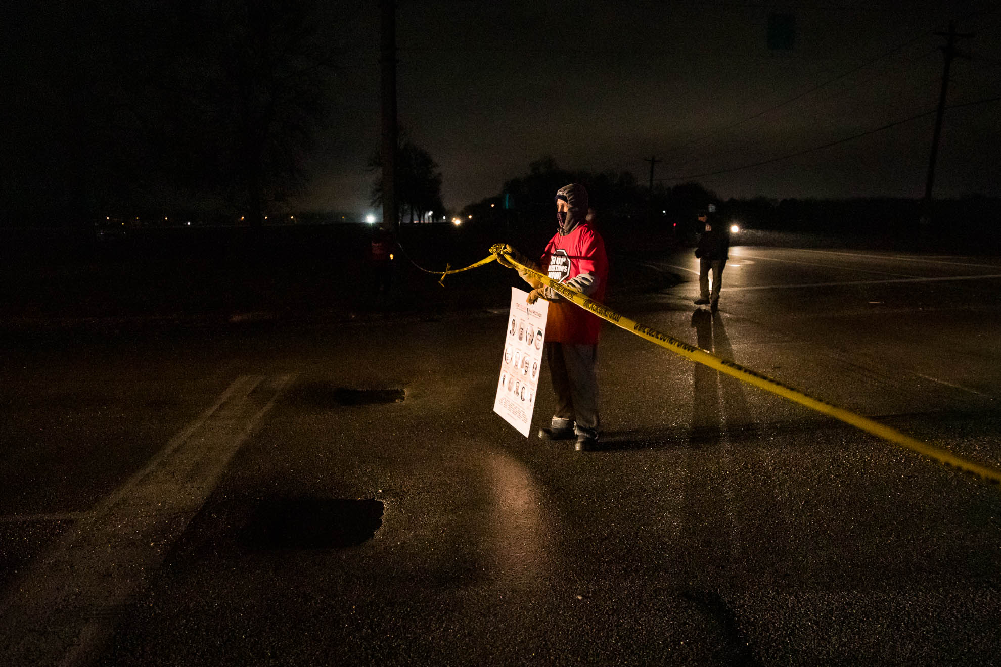 A protestor blocks the main driveway entrance to the prison with “crime scene” tape